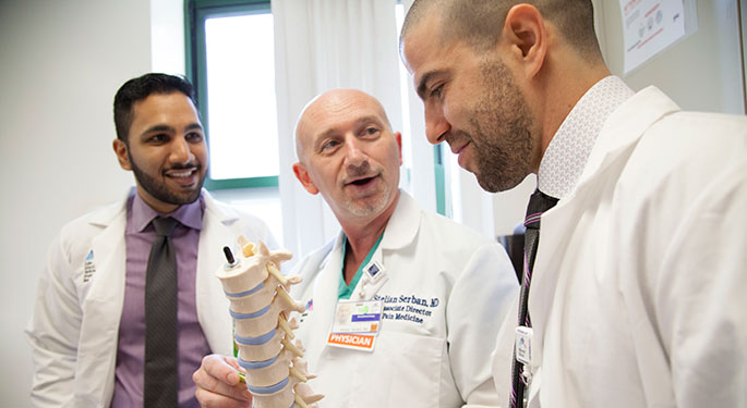 Three male doctors discuss a model of the spine