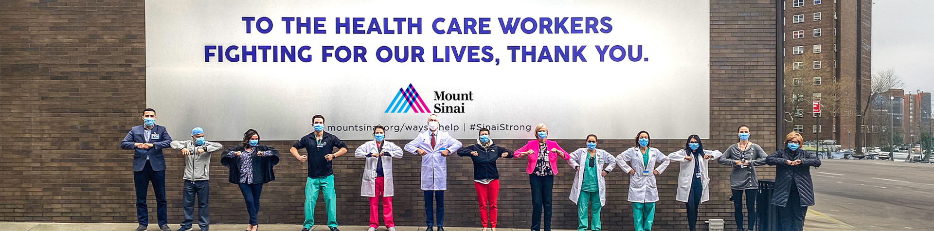 masked healthcare workers in front of oversized To the Health Care Workers Fighting for Our Lives, Thank you banner 